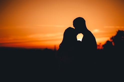 Beautiful young woman and her boyfriend in a silhouette kissing in the field at sunset.