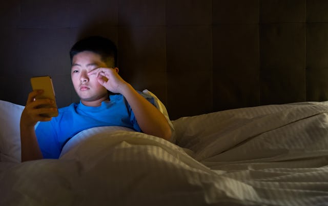 Teenage boys using mobile phone in bed. A new survey shows most high school students are not getting...