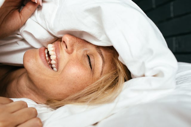 Portrait of a young beautiful woman waking up among the bed sheets, with a smile on her face