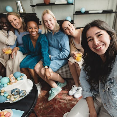 A multiracial group of female friends posing for a selfie at a baby shower celebration. They are looking at the camera and hugging each other. Creating memories together.