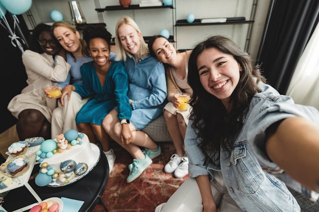 A multiracial group of female friends posing for a selfie at a baby shower celebration. They are loo...