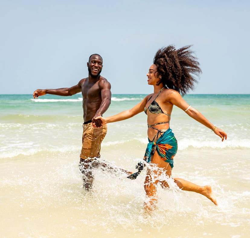 Happy couple enjoying a sunny day at the beach, splashing through the waves. Capturing the essence o...
