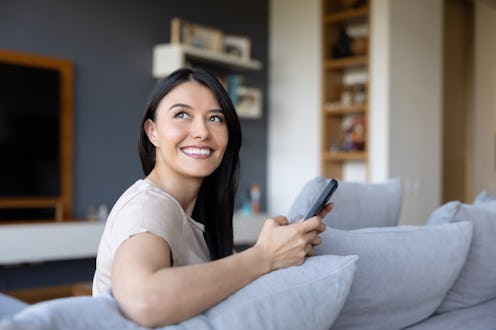 Portrait of a happy Latin American woman at home using an app on her mobile phone