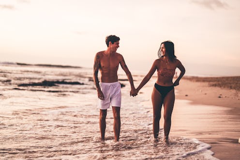 Couple holding hands while walking along a sandy beach during sunset, enjoying a romantic and carefr...