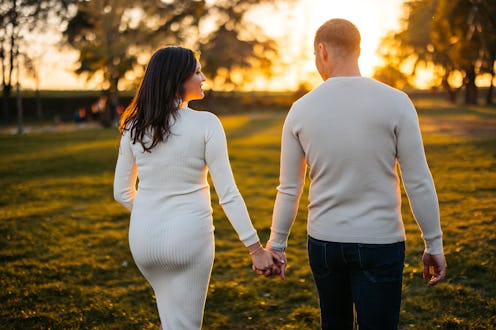 Rear-view of a beautiful young woman and her boyfriend walking in the field at sunset.