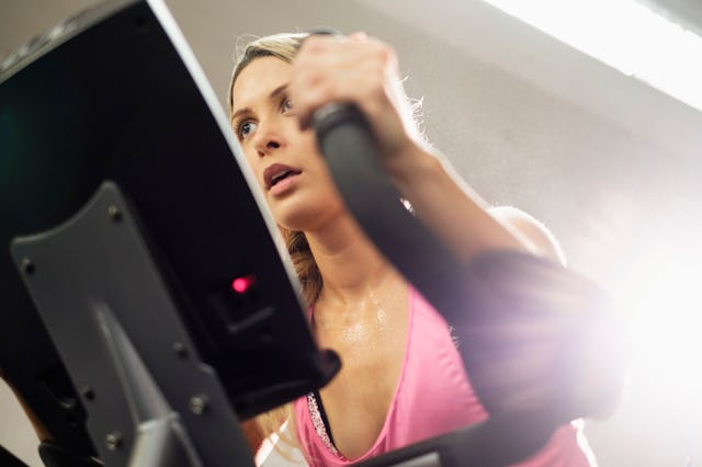 A focused woman exercising on an elliptical machine in a gym. She appears determined, with a light s...