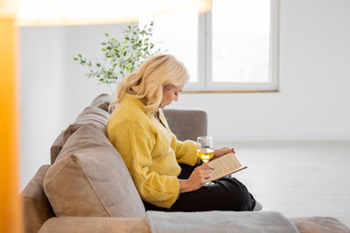 Woman At Home Sitting On Bed Reading Book And Drinking Wine