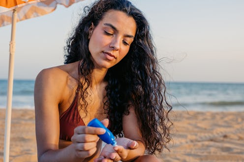 Young woman applying sunscreen while sitting on the beach in Barcelona in Spain.