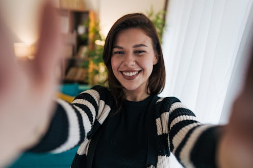 Young woman with long brown hair, wearing a striped cardigan, smiling and stretching her arms wide w...
