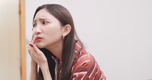 Closeup side view young asian businesswoman looks in mirror and is dissatisfied with her facial poor...