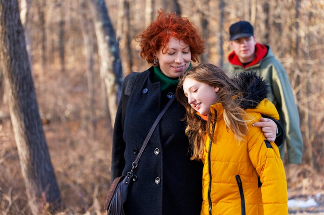 A 46-year-old red-haired woman gently embraces her 10-year-old daughter, sharing a warm, affectionat...