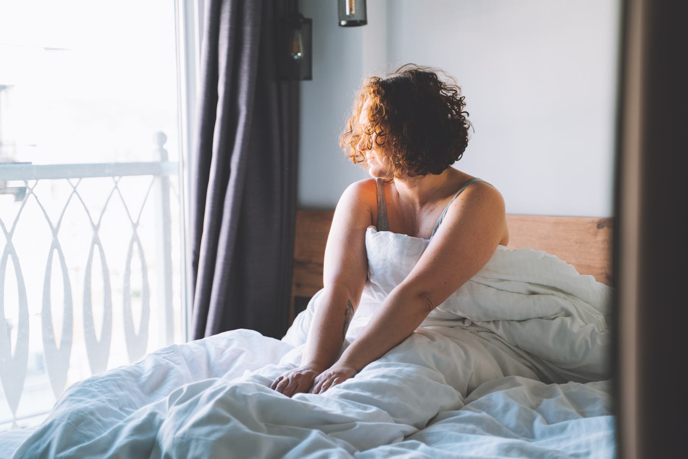Good morning weekend. Middle age curly woman wake up and sit in bed looking to the window