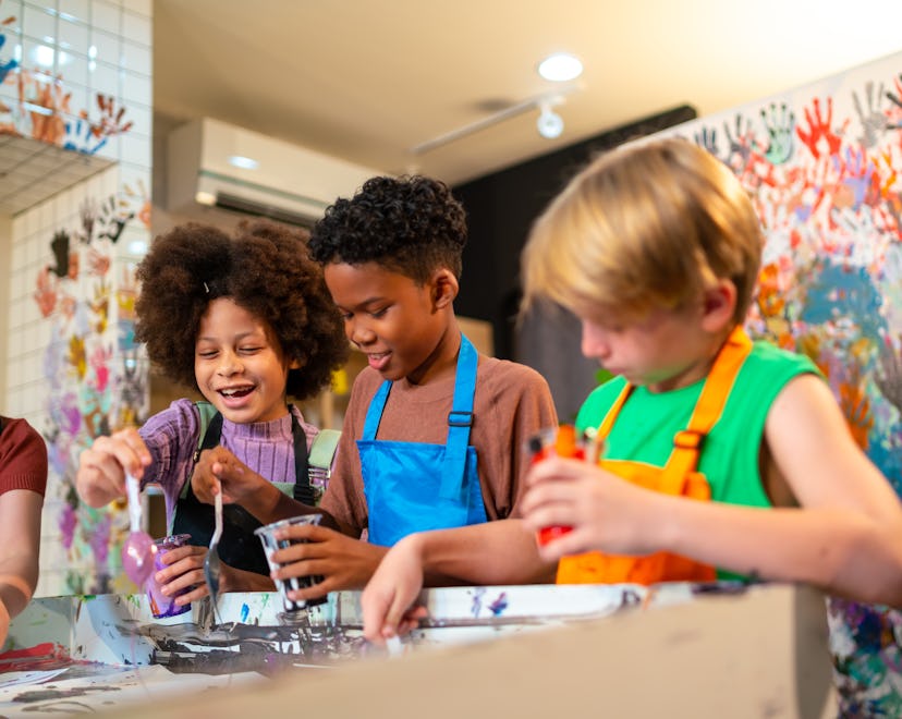 Group of Diversity school children learning acrylic pouring art on canvas workshop with teacher at a...