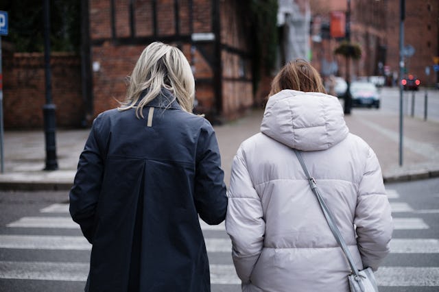 Rear view of two mature ladies, blonde carrying cup of coffee in hand and brunette with crossbody ba...