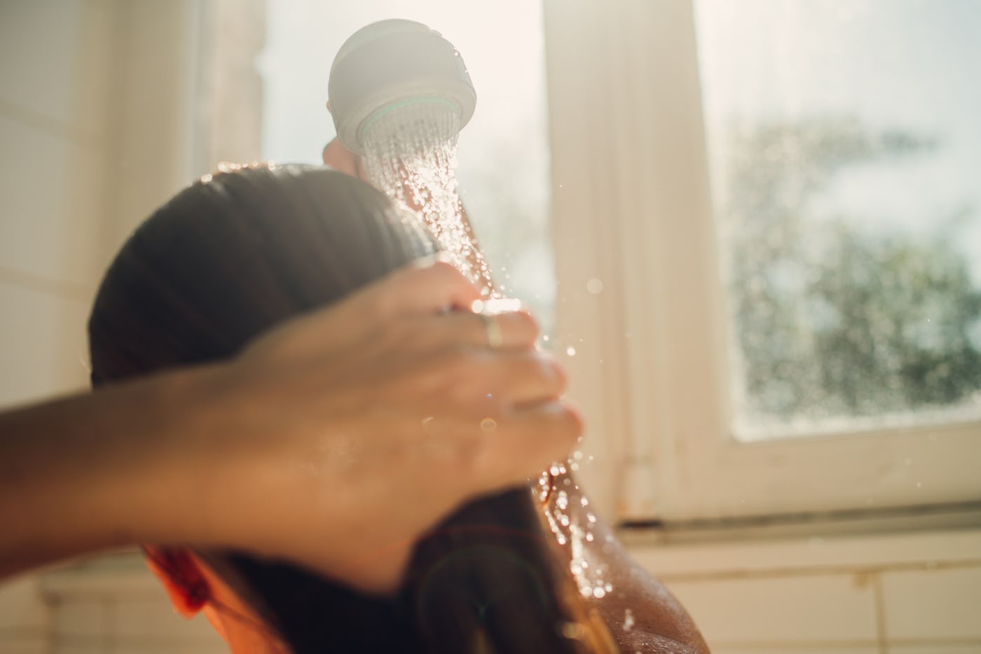 Woman washing hair with shampoo at a bright sunny day.