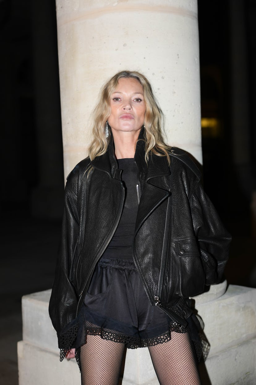 Kate Moss wears silver earrings, black sweater, shiny black oversized blazer leather jacket, shiny s...