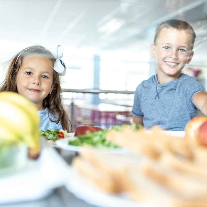Two children look at the camera over a spread of healthy food in a school cafeteria.