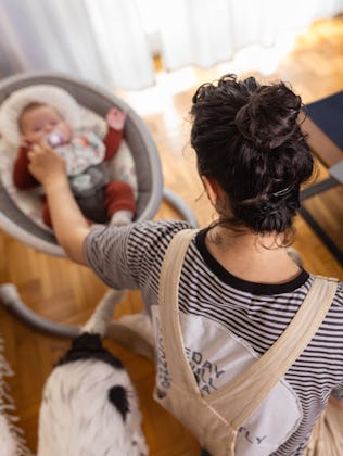A mother using her laptop while her baby sleeps soundly in a nearby swing.