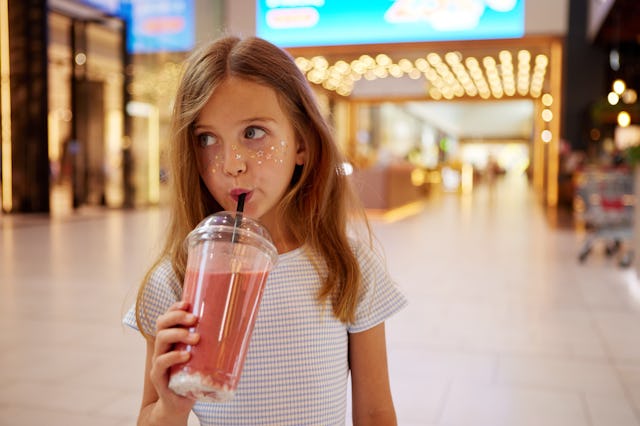 A young girl is leisurely sipping on a refreshing strawberry milkshake as she walks through a bustli...
