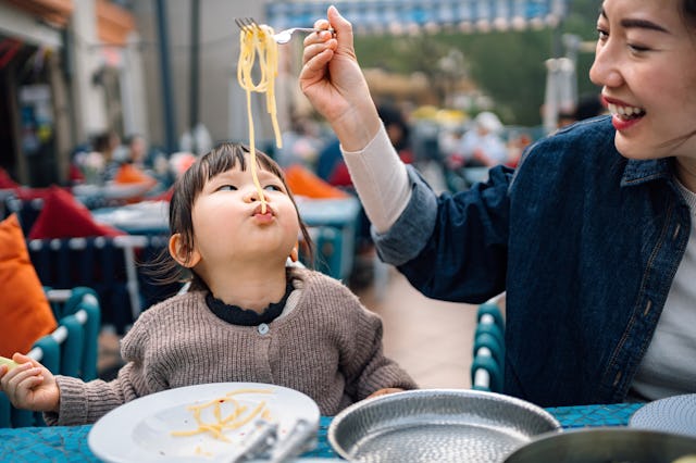 Young Asian mother and little girl having a nice time at lunch together in outdoor restaurant. Playf...
