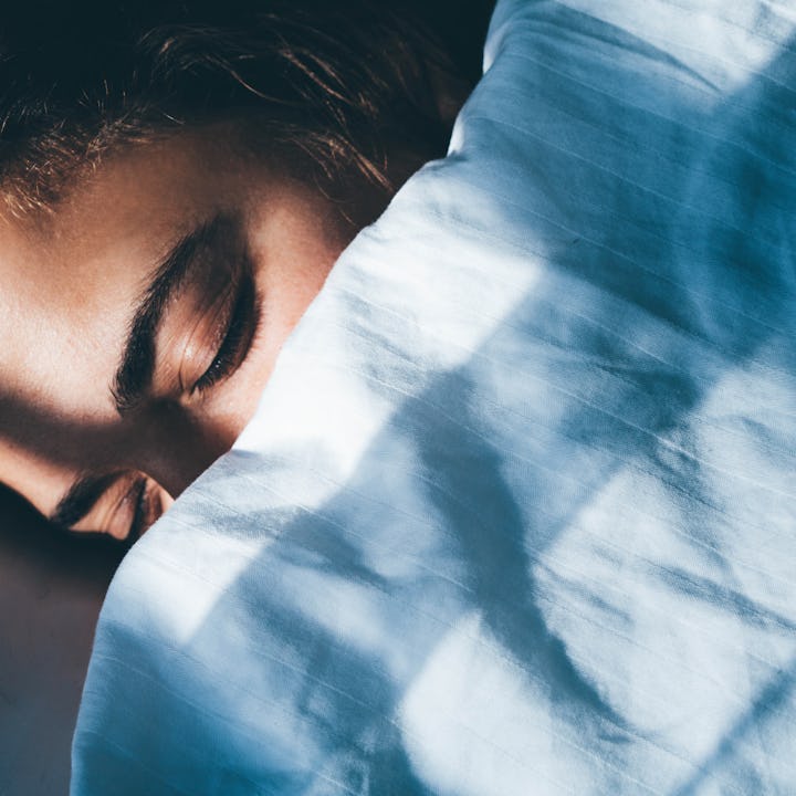 Young woman with curly hair sleeps in bed tossing and turning in dream covered with soft blanket in ...