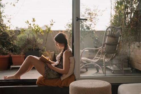 Photo of a young woman making an entry into her diary, while sitting on her apartment's terrace on a...