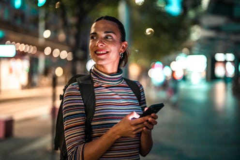 A curious Hispanic woman with a striped top and backpack explores Sydney's vibrant streets at night,...