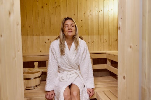 Smiling woman in bathrobe spending relaxing time in sauna. Copy space.