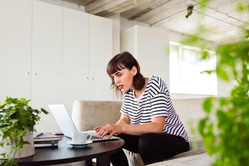 Young woman wearing striped t-shirt sitting on sofa in the creative workplace and using laptop.
