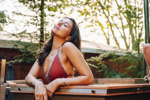 Spa retreat. A joyful woman with eyes closed in a bikini leans on the edge of a hot tub, enjoying th...