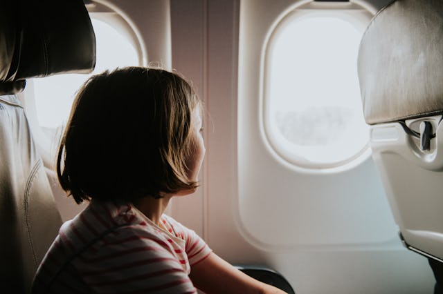 A young girl sits by the airplane window, watching the scenery change outside, her curious expressio...