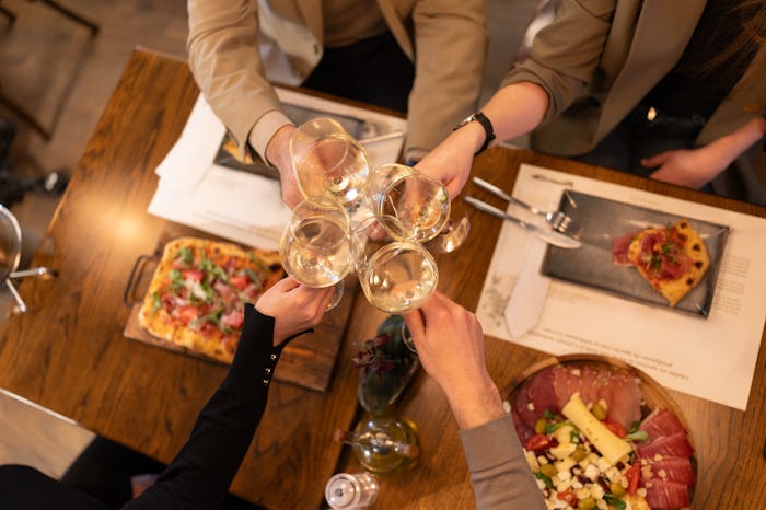 High angle shot of four unrecognizable persons toasting with white wine over diner in luxury restaur…