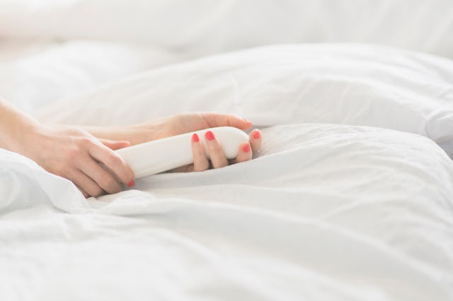 A woman's hand holds a nondescript white vibrator, in a story about common mistakes you might be mak...