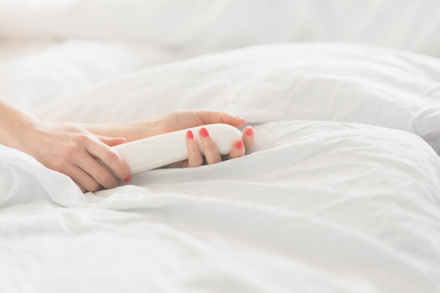 A woman's hand holds a nondescript white vibrator, in a story about common mistakes you might be making with your sex toys.