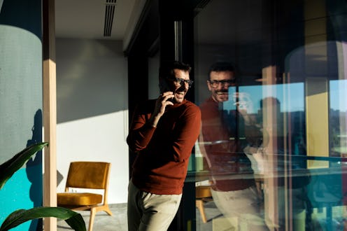 Mid adult businessman standing and talking/texting on the smart phone telephone in the modern office