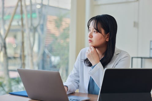Confident Asian female medical professional is using a laptop.