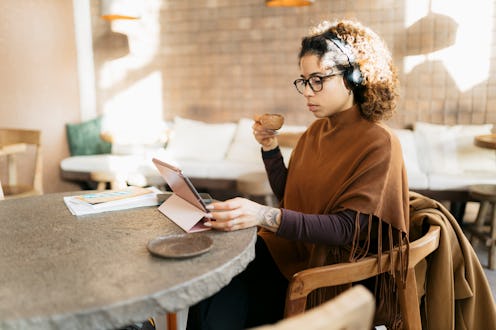 Young adult freelancer working remotely using digital tablet, enjoying latte and listening to music ...