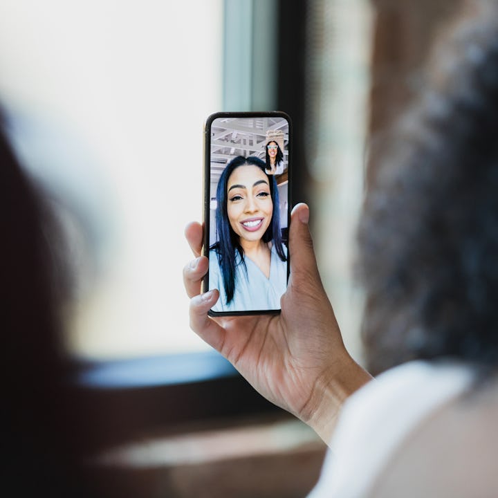 Two unrecognizable women use a teleconferencing app on a smart phone to meet with a female colleague...