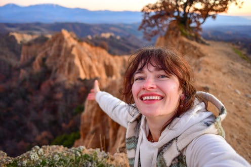 Female solo traveler sitting on top of a mountain enjoying beautiful morning view over the valley