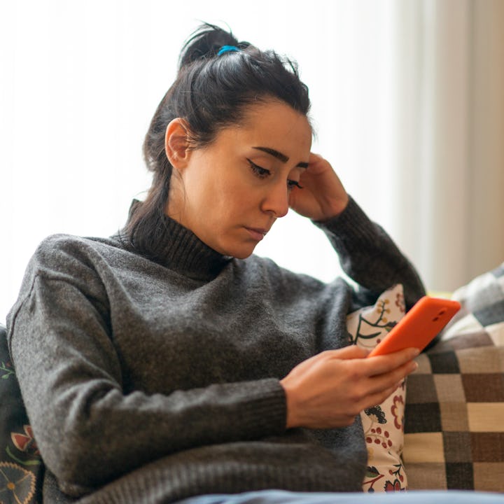 Woman sitting on a sofa and looking at mobile phone screen at home.