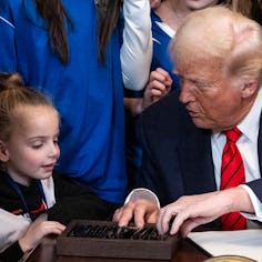 US President Donald Trump speaks with a little girl as he selects a pen to sign the No Men in Women'...
