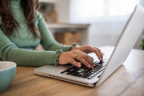 Happy businesswoman working remotely from her home, sitting comfortably at the kitchen table, typing...