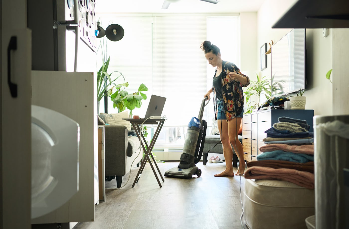 Young woman vacuuming her living room floor while doing laundry and chores around the home at the weekend