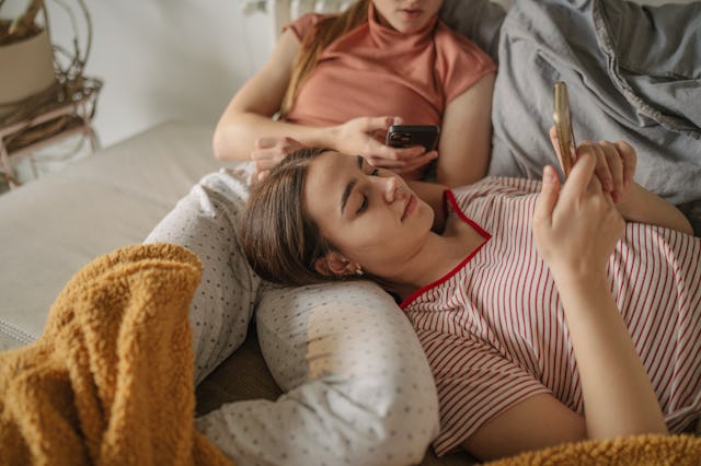 Two teen girls hang out while looking at their phones.