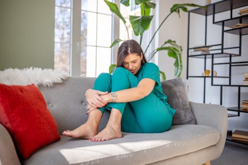 A female nurse at home, showing signs of discomfort and distress as she struggles with pain.