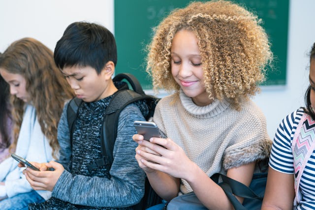 A group of middle school students is sitting in a row on the desks in their classroom. All of the st...