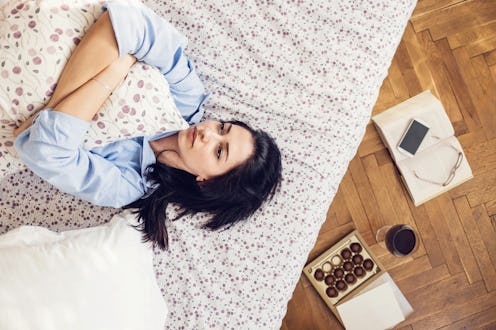 Beautiful sad female wearing male shirt, hugging pillow and lying down on her bed
