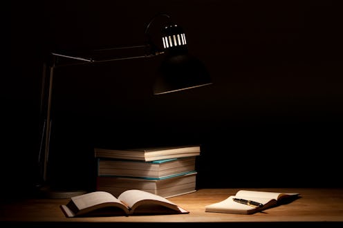 Low Key image of a table with lamp, books and sketchpad.