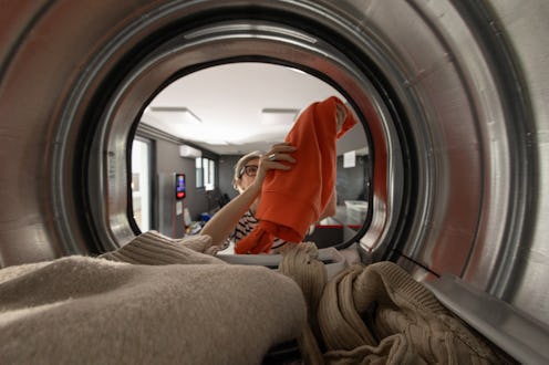 Mature woman taking dry clothes out of machine in self-service public laundry, photo taken from ins...