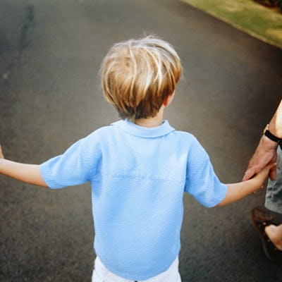 A young child wearing a light blue shirt walks on a path, holding hands with adults on either side, enjoying a moment of togetherness.